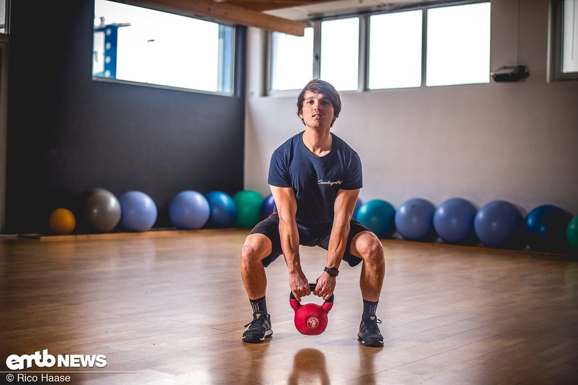 Wer keine Langhantel zur Verfügung hat, kann die effiziente Übung auch mit der Kettlebell durchführen. In Ausgangsposition die Arme gerade zwischen den Beinen nach unten "fallen" lassen...